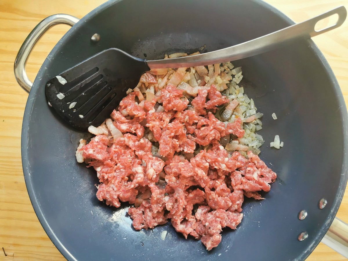 Crumbled sausage meat in skillet with diced onion and guanciale.
