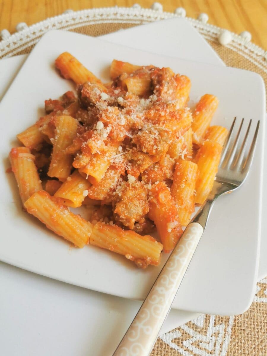 Sausage rigatoni pasta alla zozzona on white plate with grated Pecorino on top.