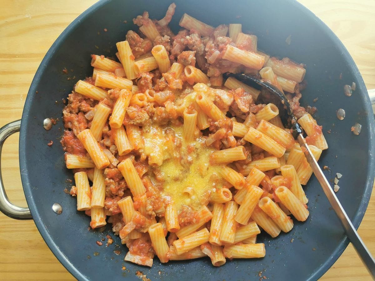 Egg yolks mixed with pecorino added to cooked rigatoni with sausage ragu in skillet.