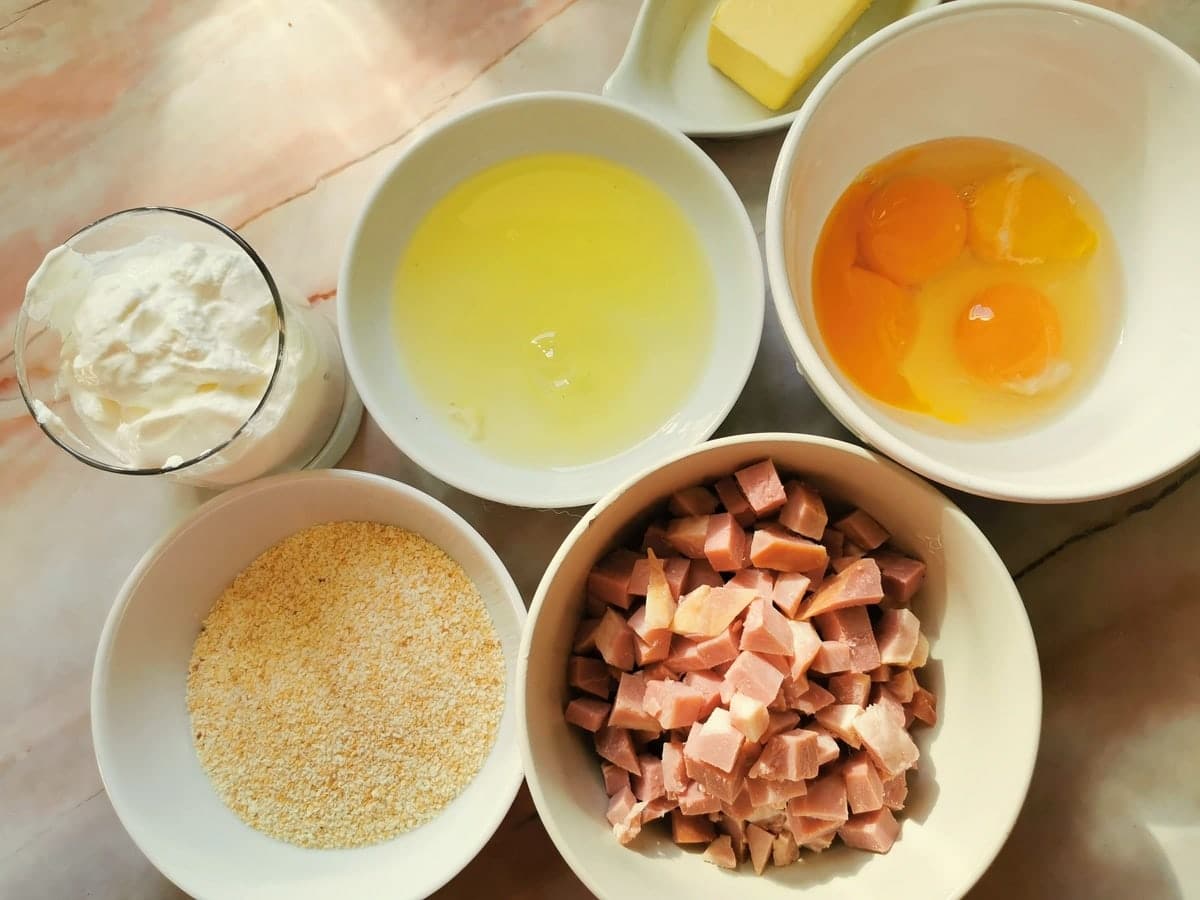 Chopped ham, egg yolks, egg whites, sour cream and breadcrumbs in separate small white bowls.