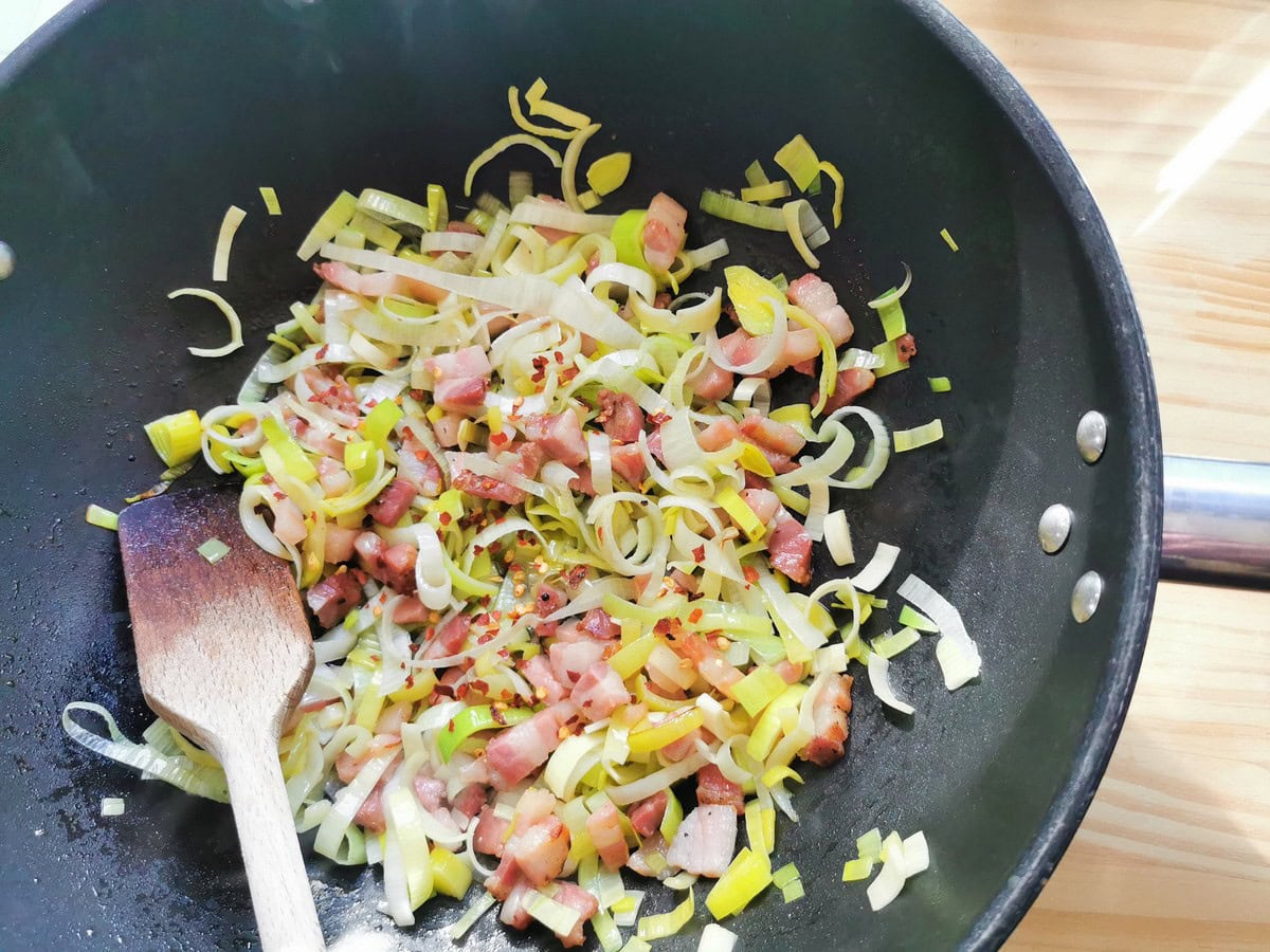 Dried chili flakes added to pancetta and leeks in skillet.