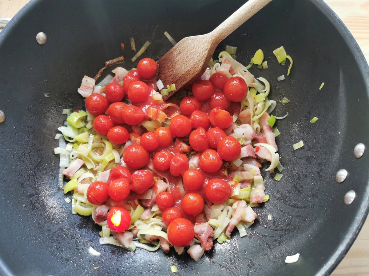 Canned cherry tomatoes added to cooked pancetta and leeks in skillet.