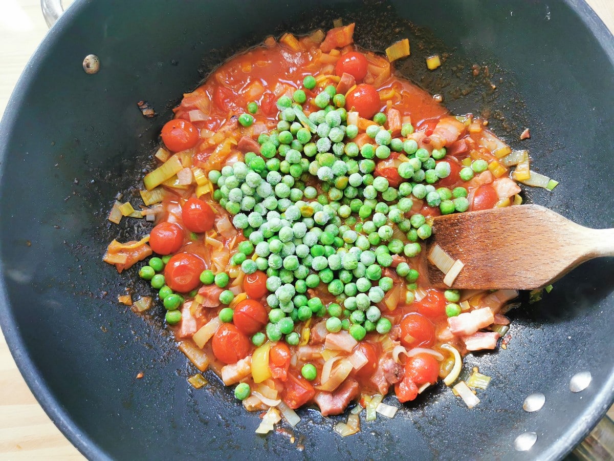 Frozen peas added to seven P pasta sauce cooking in skillet.