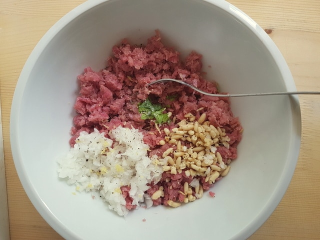 ground fresh tuna, finely chopped onions, pine nuts and fresh mint in white bowl