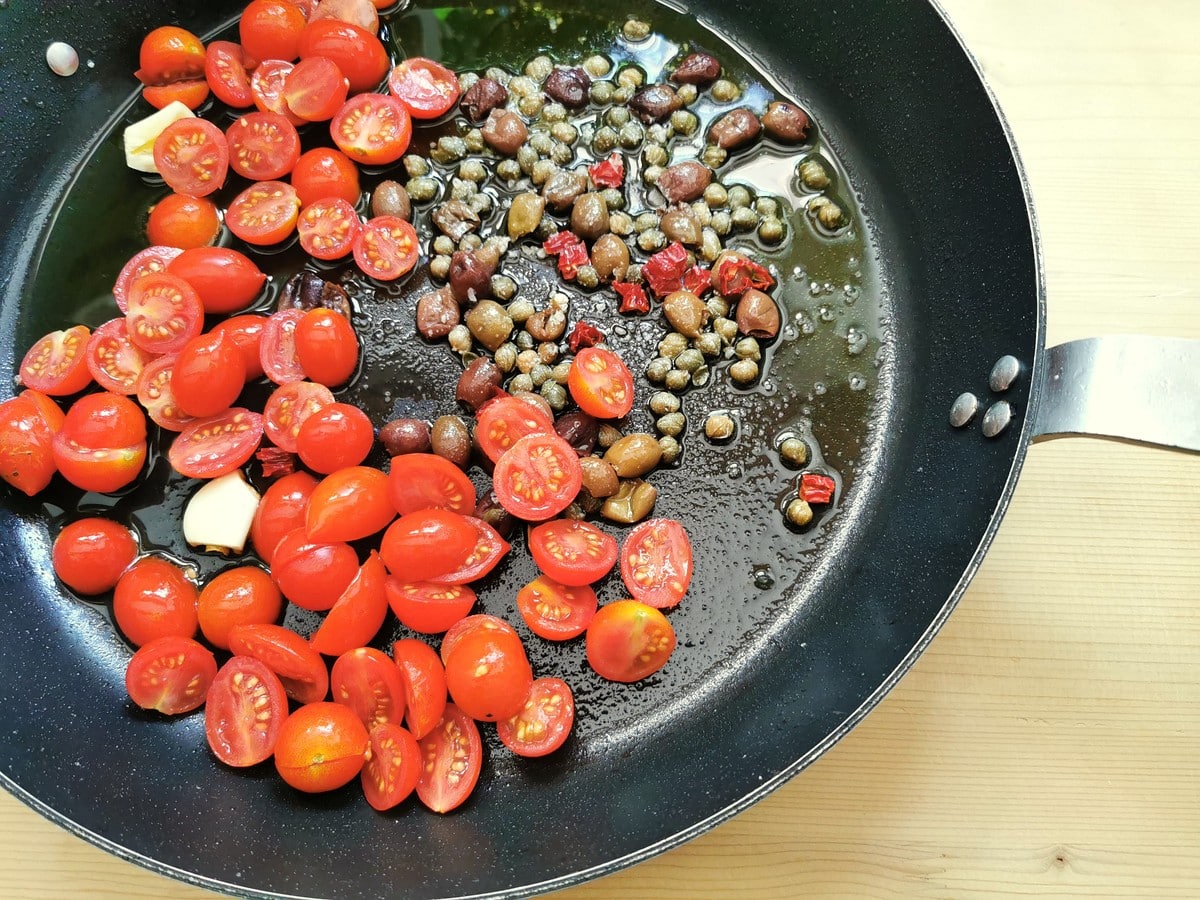 garlic, capers, olives and cut cherry tomatoes in skillet