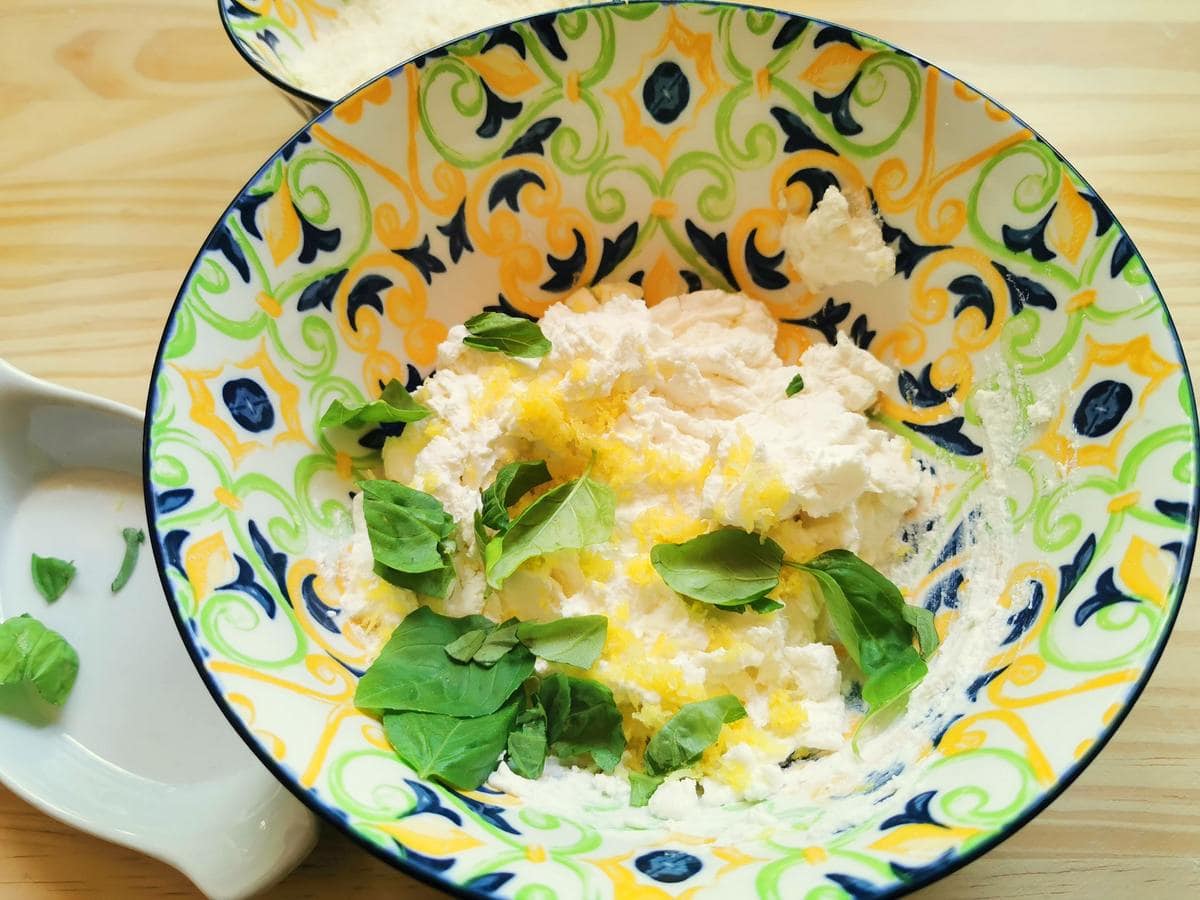 A large bowl with ricotta lemon zest and basil leaves