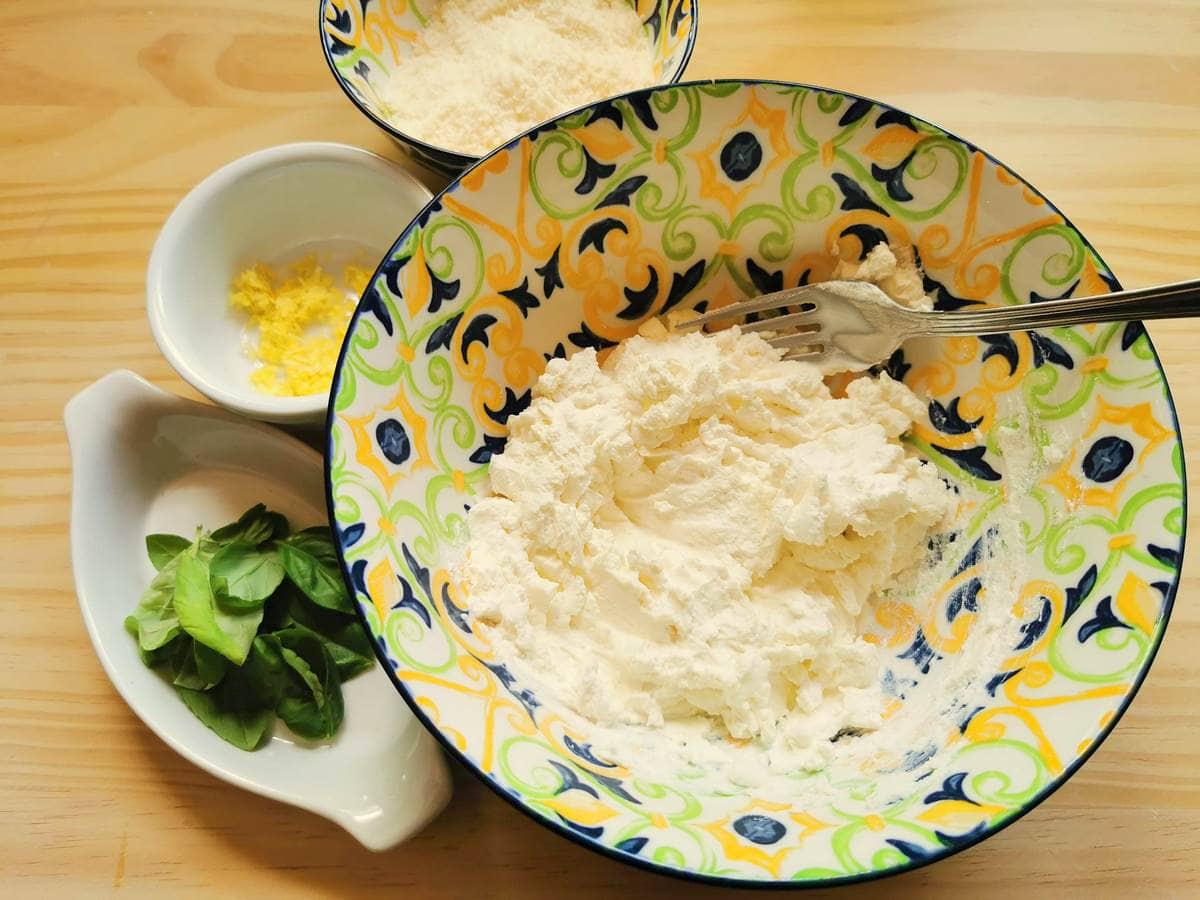 Mashed fresh ricotta with fork in blue and yellow bowl