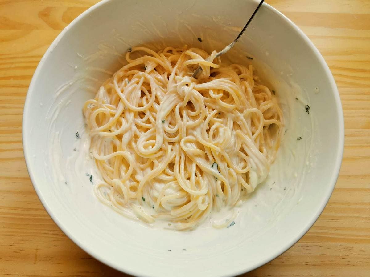 cooked spaghetti mixed with creamy ricotta sauce in white bowl