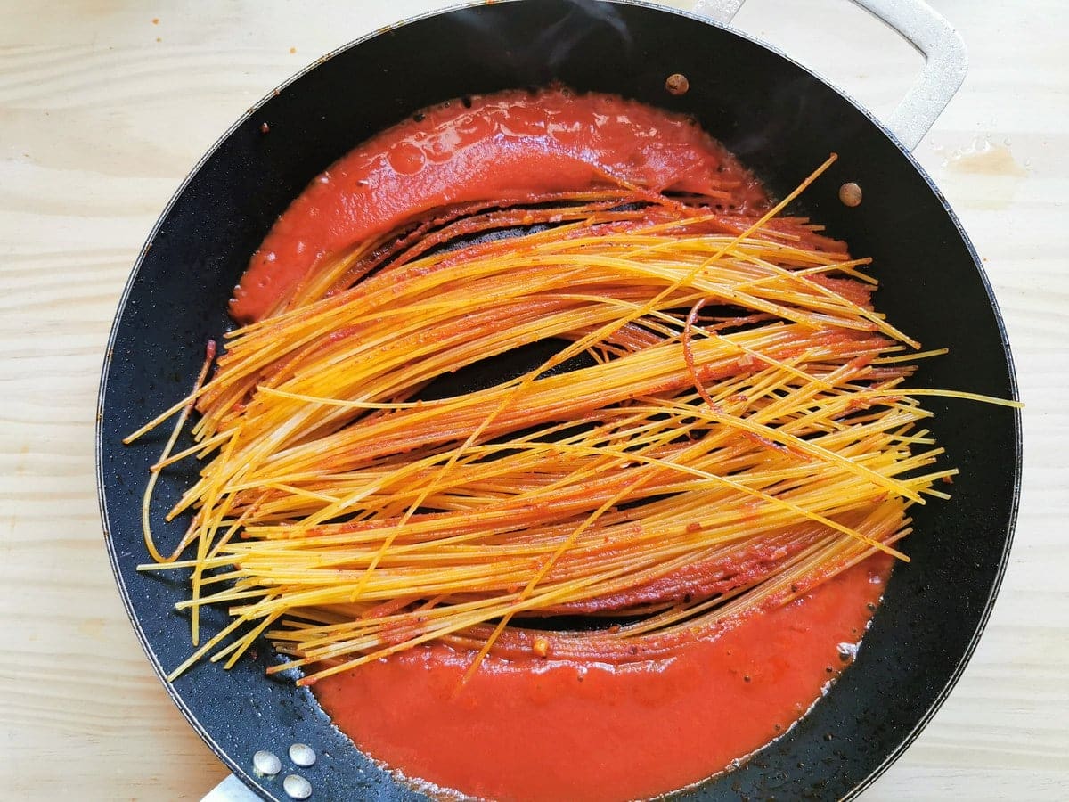 Tomato passata broth on the sides of spaghetti cooking in skillet