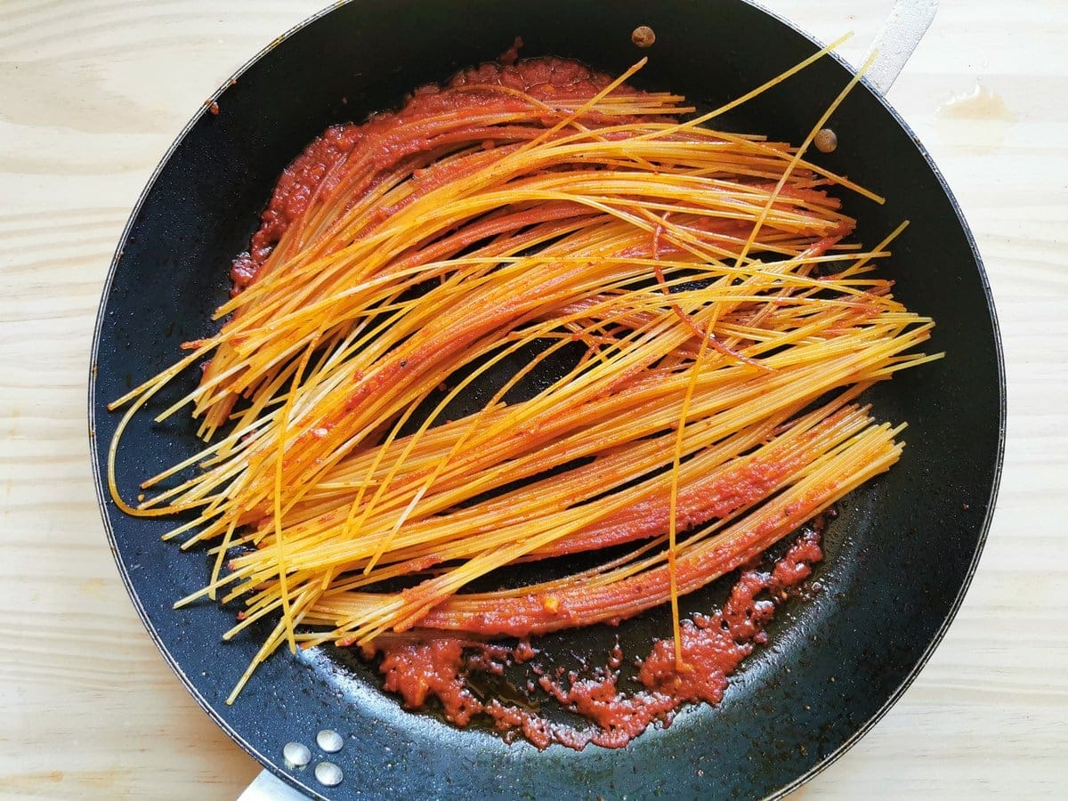 dried spaghetti starting to caramelize in skillet with tomato passata