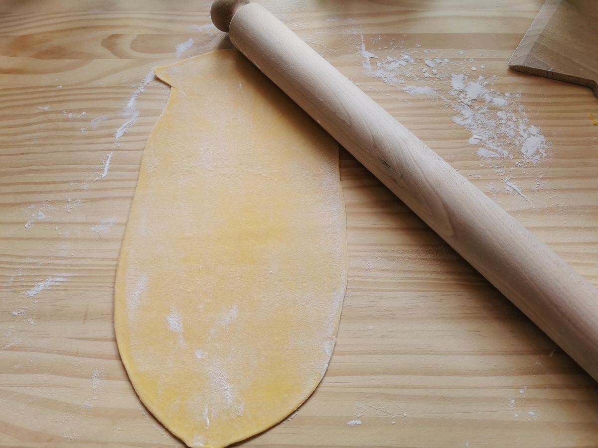 A sheet of chitarra pasta dough rolled out on wood surface with a rolling pin.