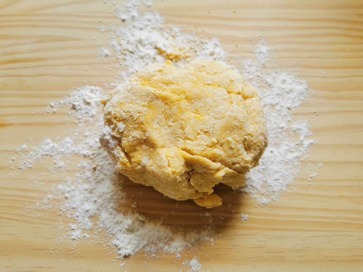 Dough ready to be kneaded on flour dusted wood work surface.