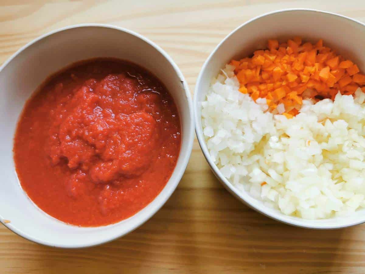 Tomato passata in a bowl and chopped onions, carrot and celery in a bowl.
