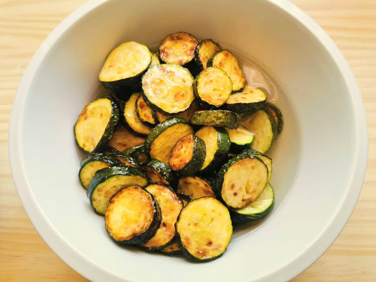 fried zucchini slices in water in white bowl.