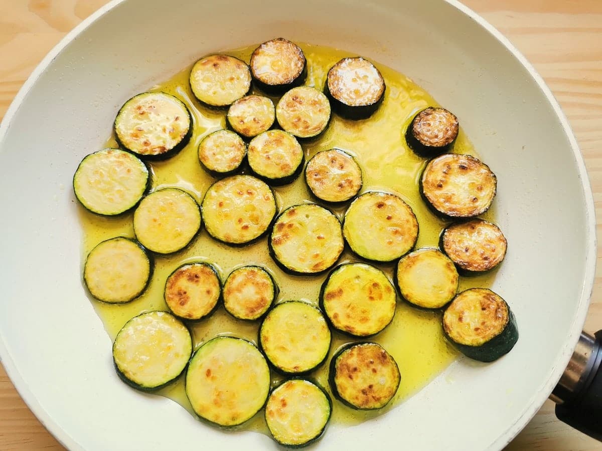 Ready fried zucchini slices in olive oil in white pan