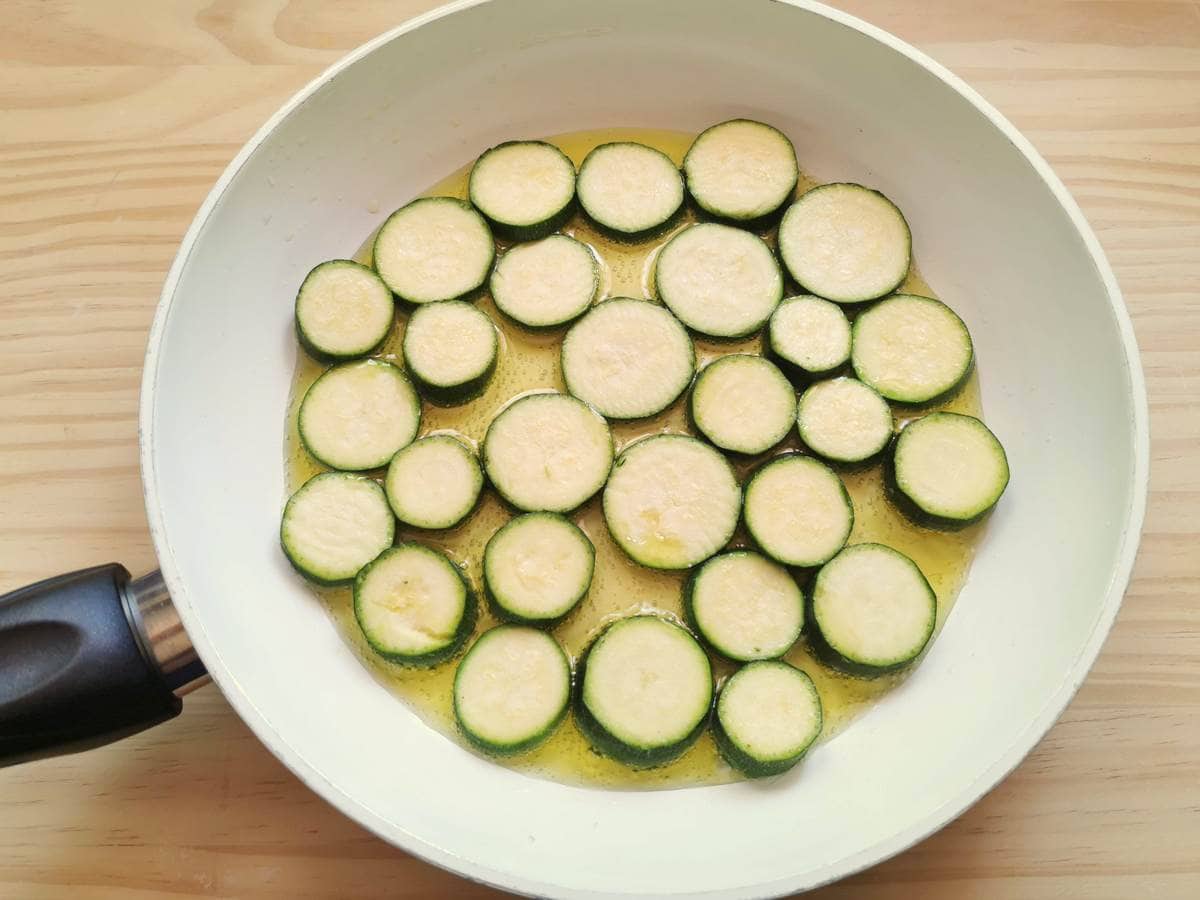 zucchini slices frying in olive oil in white pan