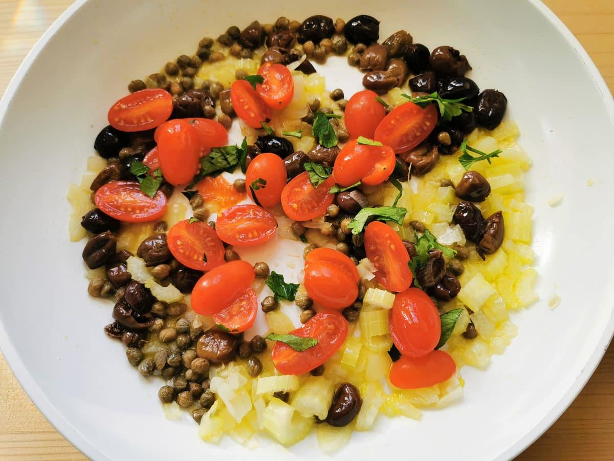 halved cherry tomatoes in pan with onions, celery, olives and capers