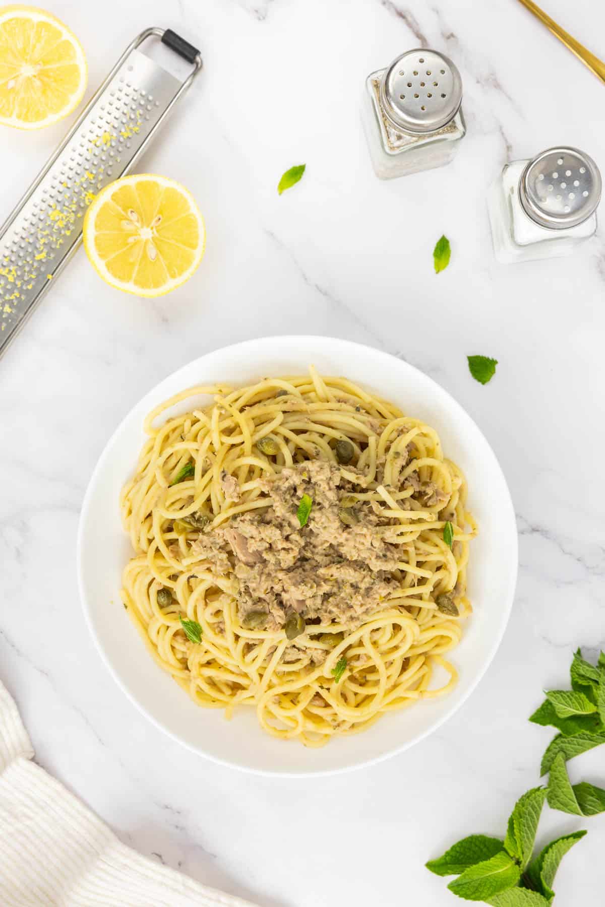 Canned tuna pasta in a bowl garnished with whole capers and mint