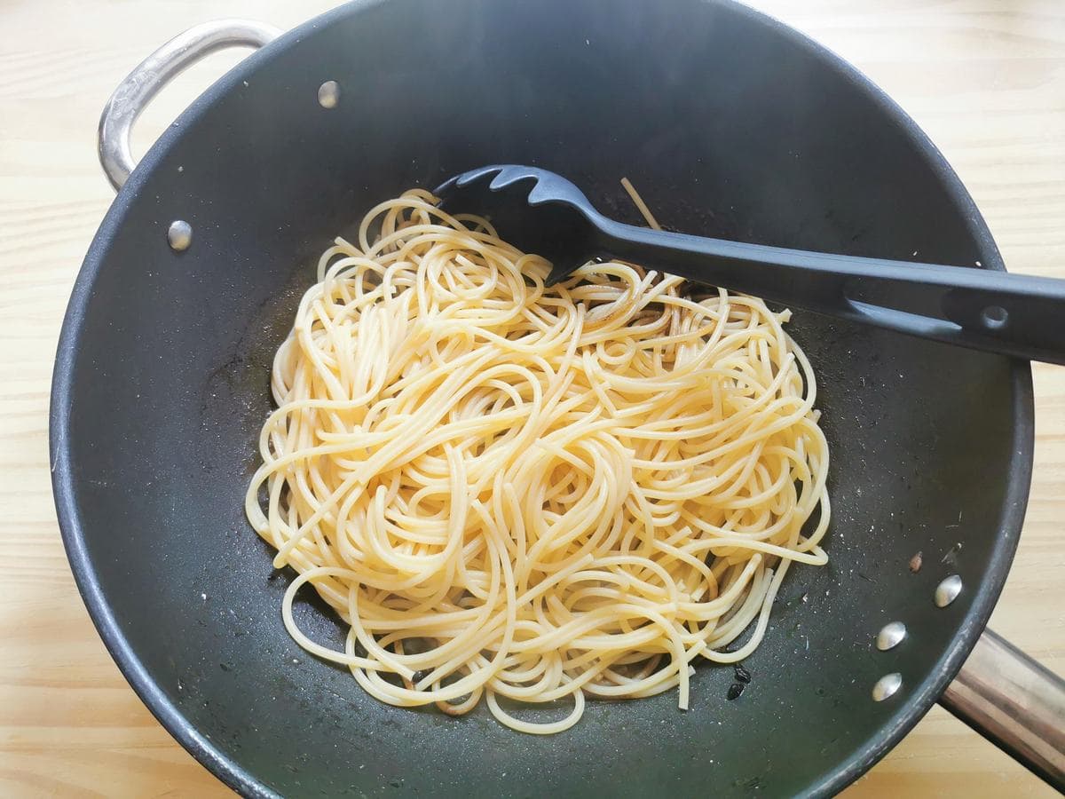 Partly cooked spaghettone in large skillet with black garlic sauce.