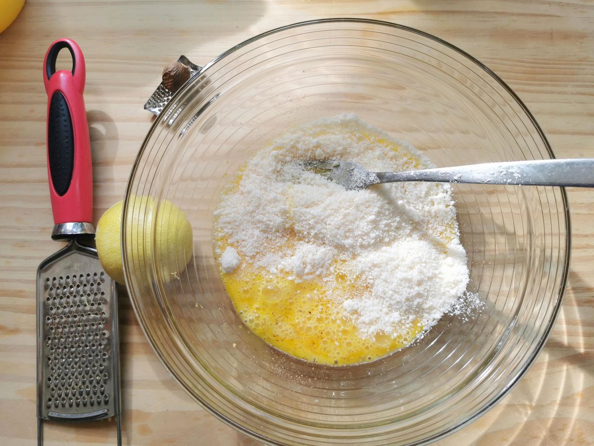 Beaten eggs with grated parmigiano in glass bowl.