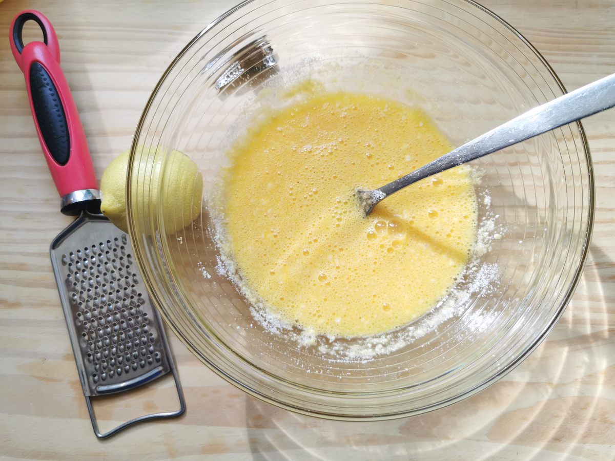 Beaten eggs mixed with grated parmigiano, grated nutmeg and lemon zest in glass bowl.
