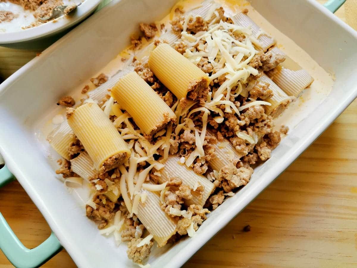 Filled paccheri pasta tubes in oven dish with ragu and cheese on top.