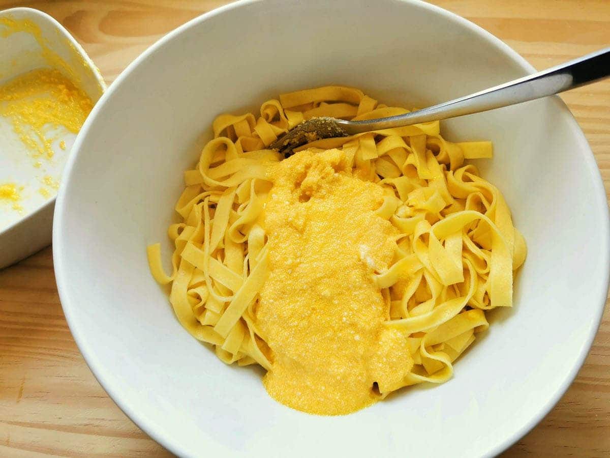 Tagliatelle being mixed with egg yolk and parmesan