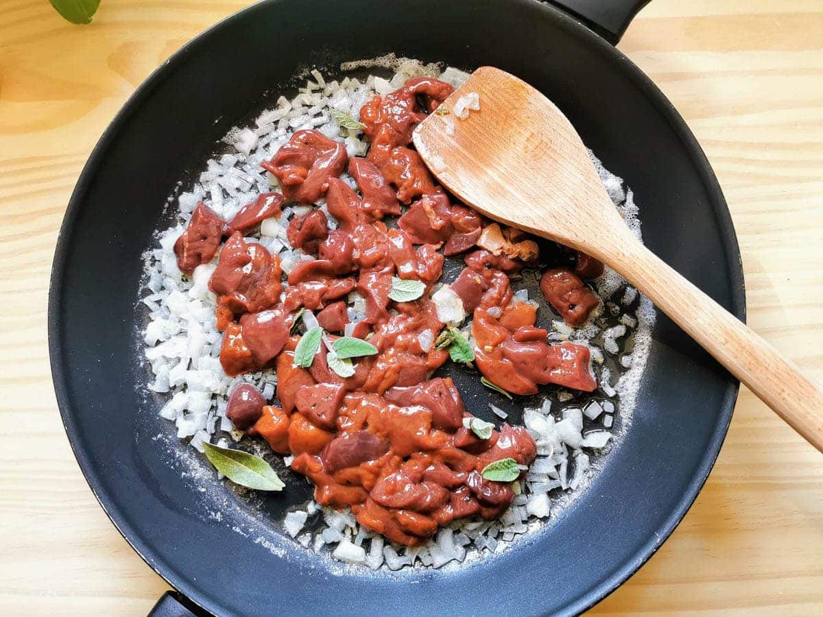 Chicken livers being cooked with onion and sage in a pan