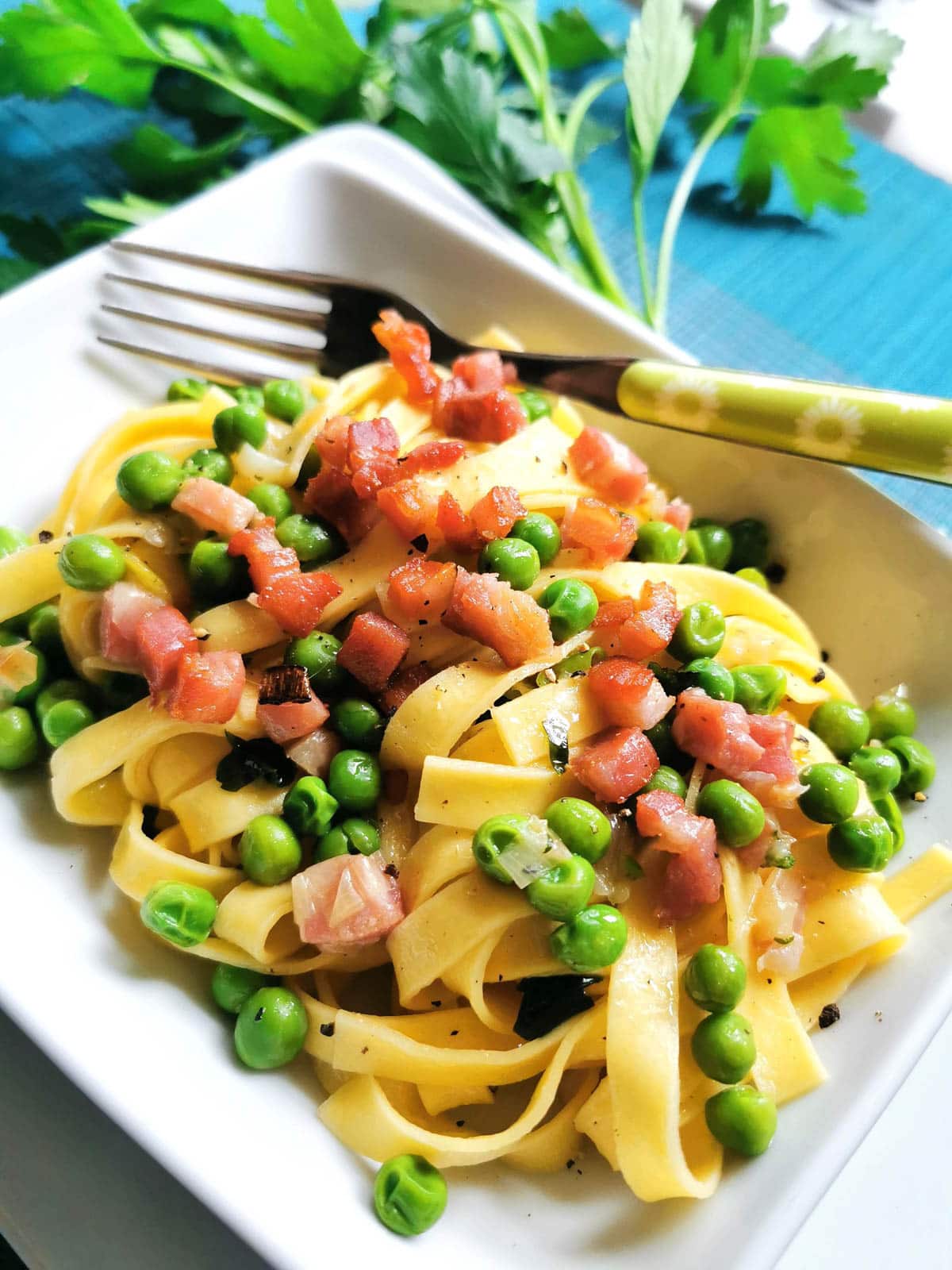 Tagliatelle pasta with peas and pancetta in a bowl with a fork.