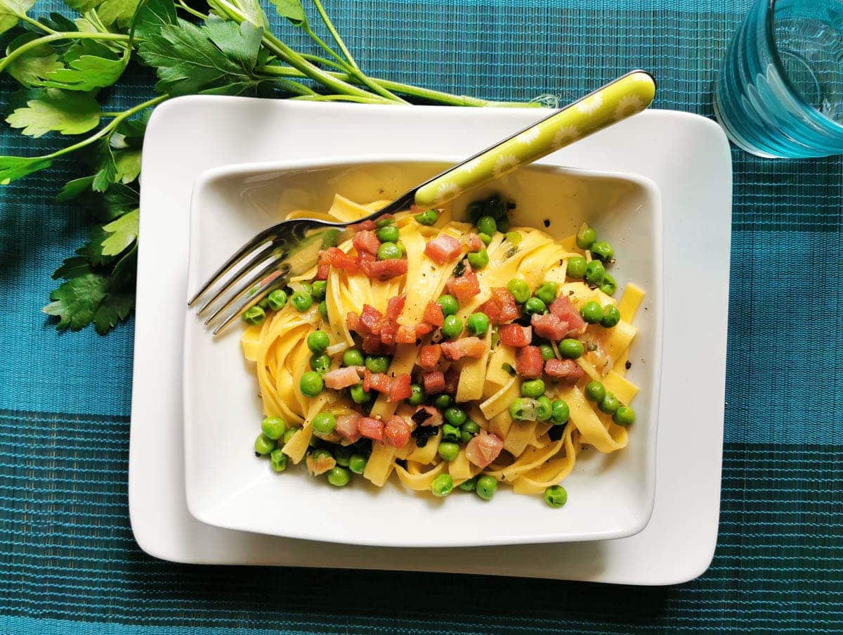 Tagliatelle pasta with peas and pancetta in a bowl with a fork.