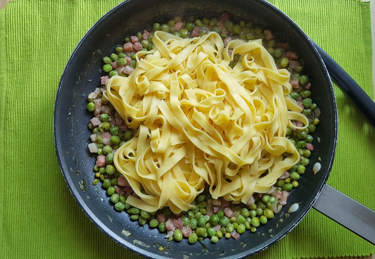 Tagliatelle added to the peas and pancetta in a frying pan