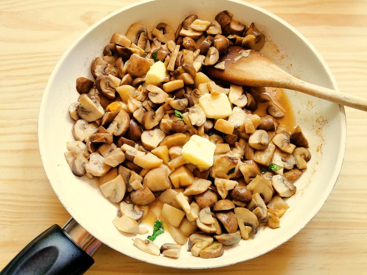 pats of butter in frying pan with porcini and cremini mushrooms