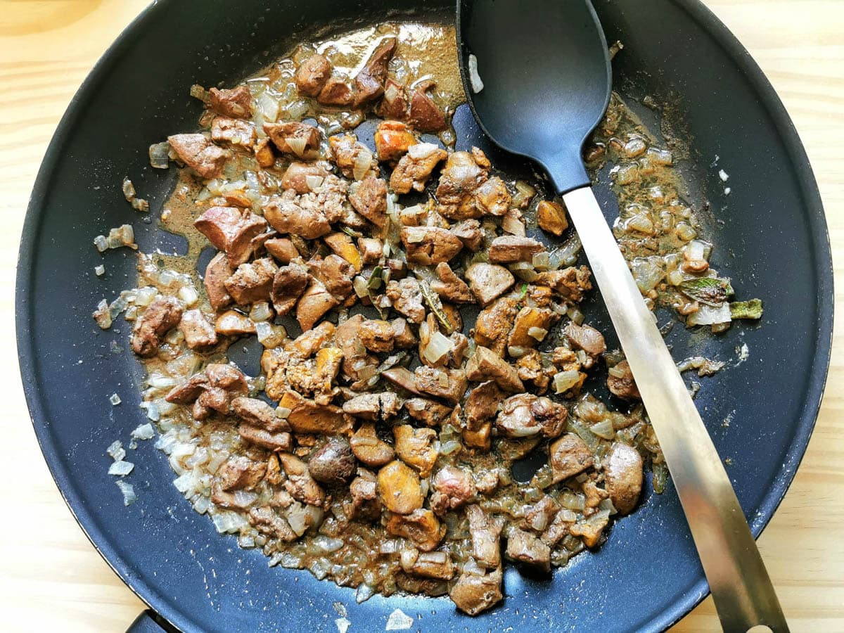 Cooked chicken livers in a pan with softened onion and sage