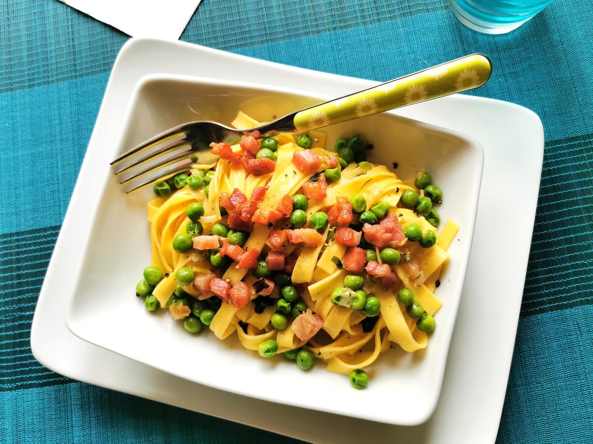 Tagliatelle pasta with peas and pancetta in a bowl on a table
