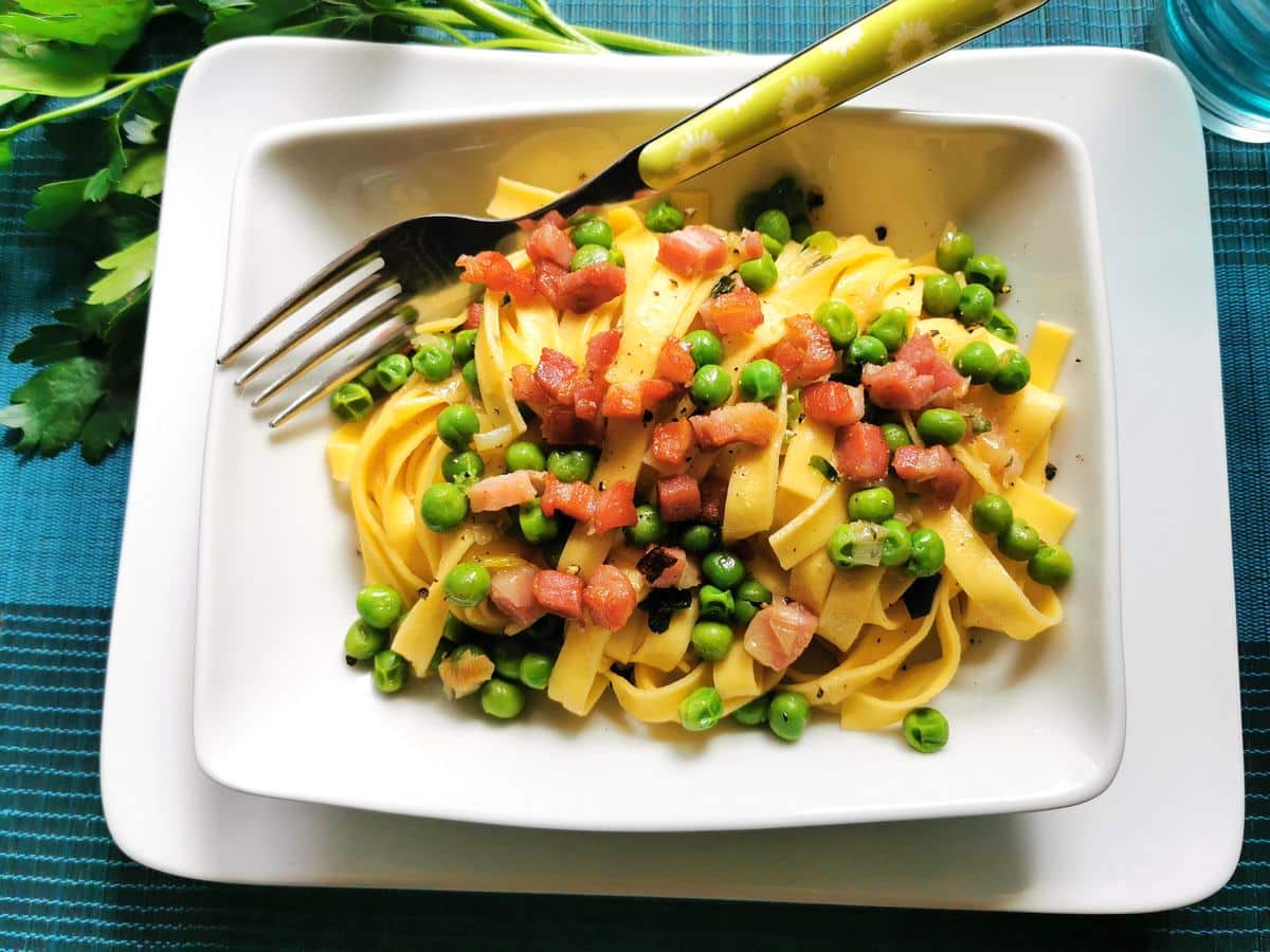 Tagliatelle pasta with peas and pancetta in a bowl with a fork.
