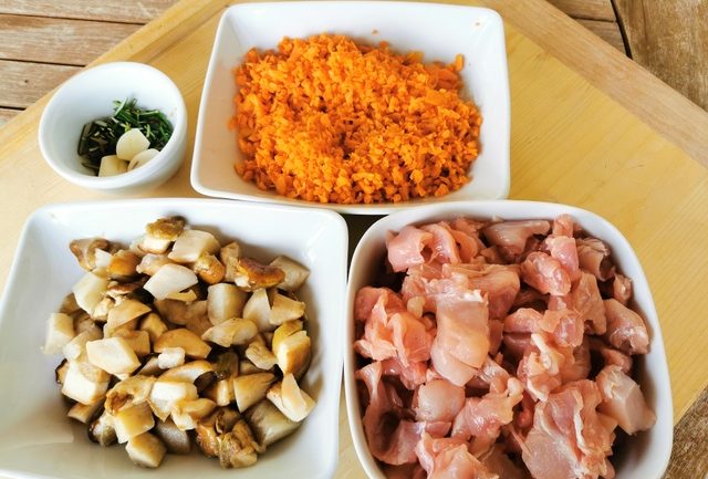 finely chopped carrots, chopped porcini, chopped parsley and peeled garlic and rabbit pieces in white bowls