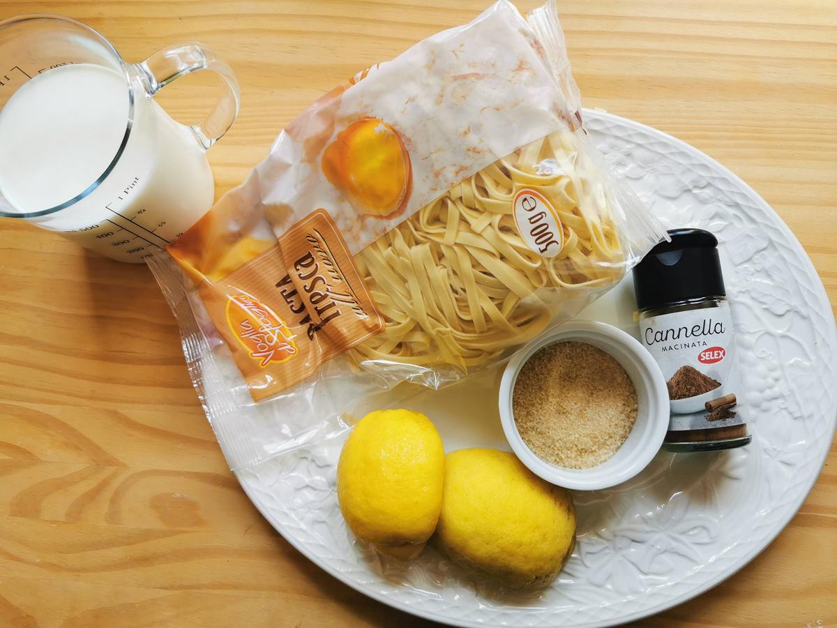 Ingredients for tagliolini in milk on white plate; fresh tagliolini, lemons, brown sugar and cinnamon powder. Plus a glass jug of fresh milk.