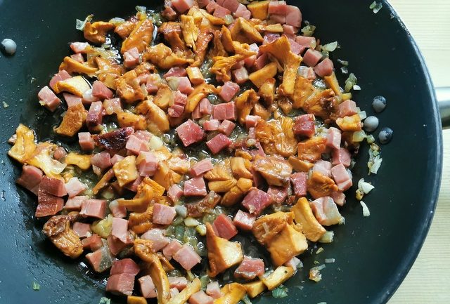 chanterelles, speck, onions and garlic cooking in skillet.