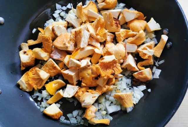 chanterelle mushroom pieces in skillet with chopped onions and garlic