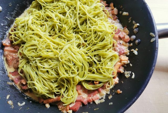 cooked spinach tagliolini in skillet with chanterelle and speck sauce