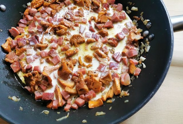 fresh cream added to chanterelle mushrooms and speck in skillet