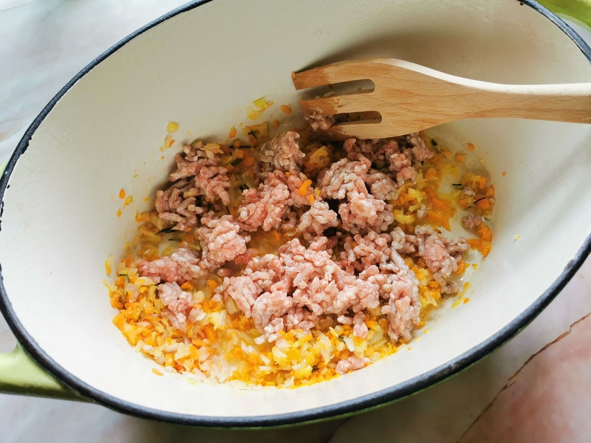 Ground veal added to chopped vegetables and herbs in Dutch oven.