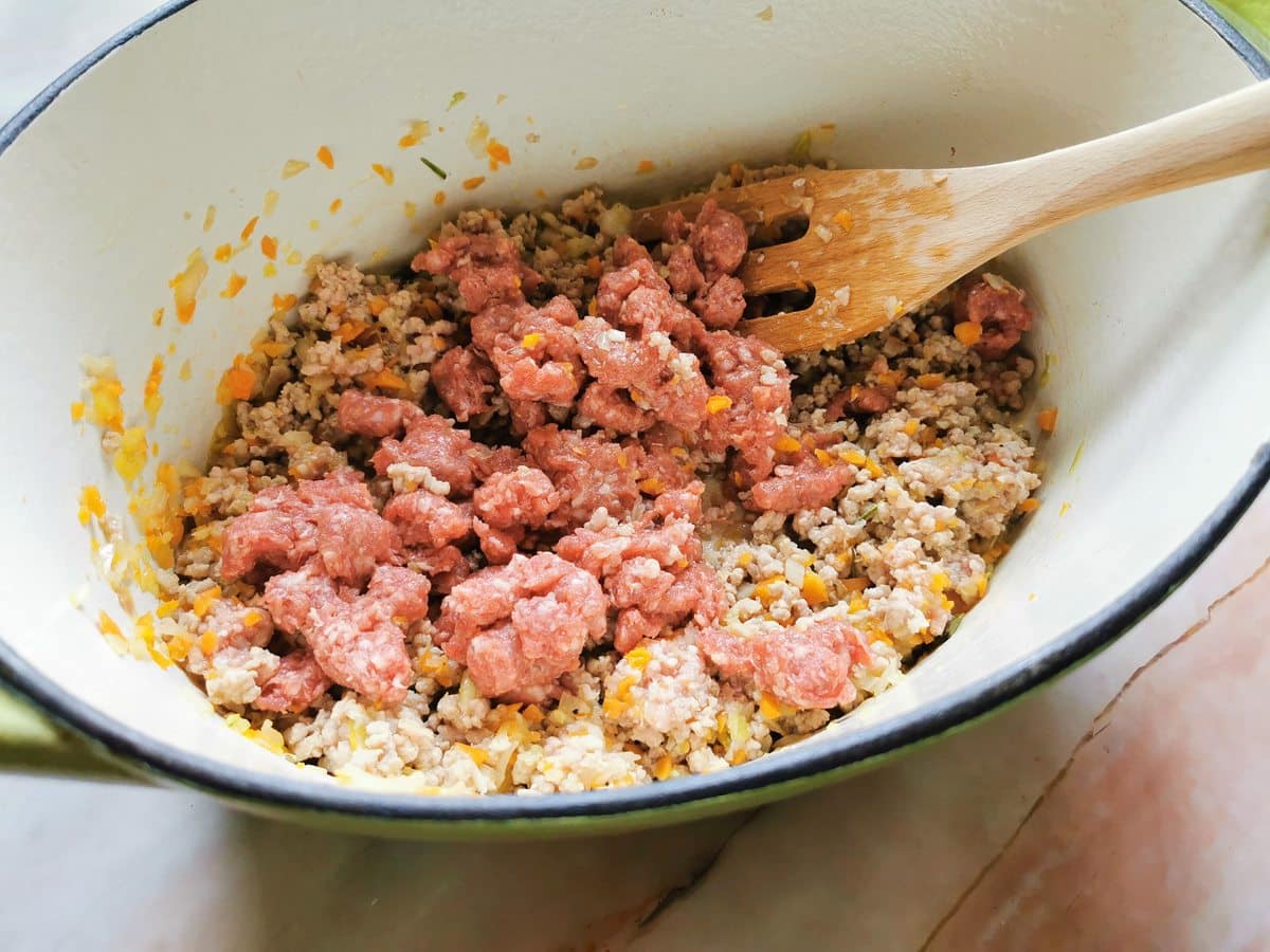 Beef sausage meat added to Dutch oven with ground veal and chopped vegetables.