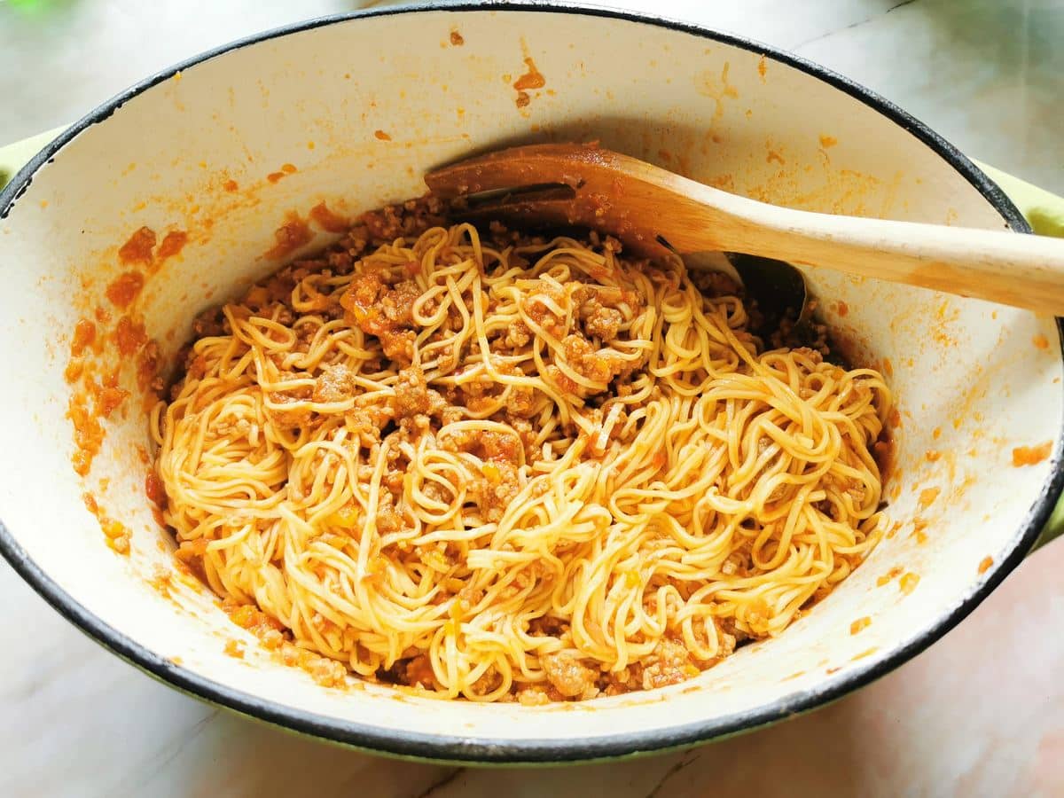 Tajarin pasta with beef sausage ragu mixed together and ready to serve in Dutch oven.