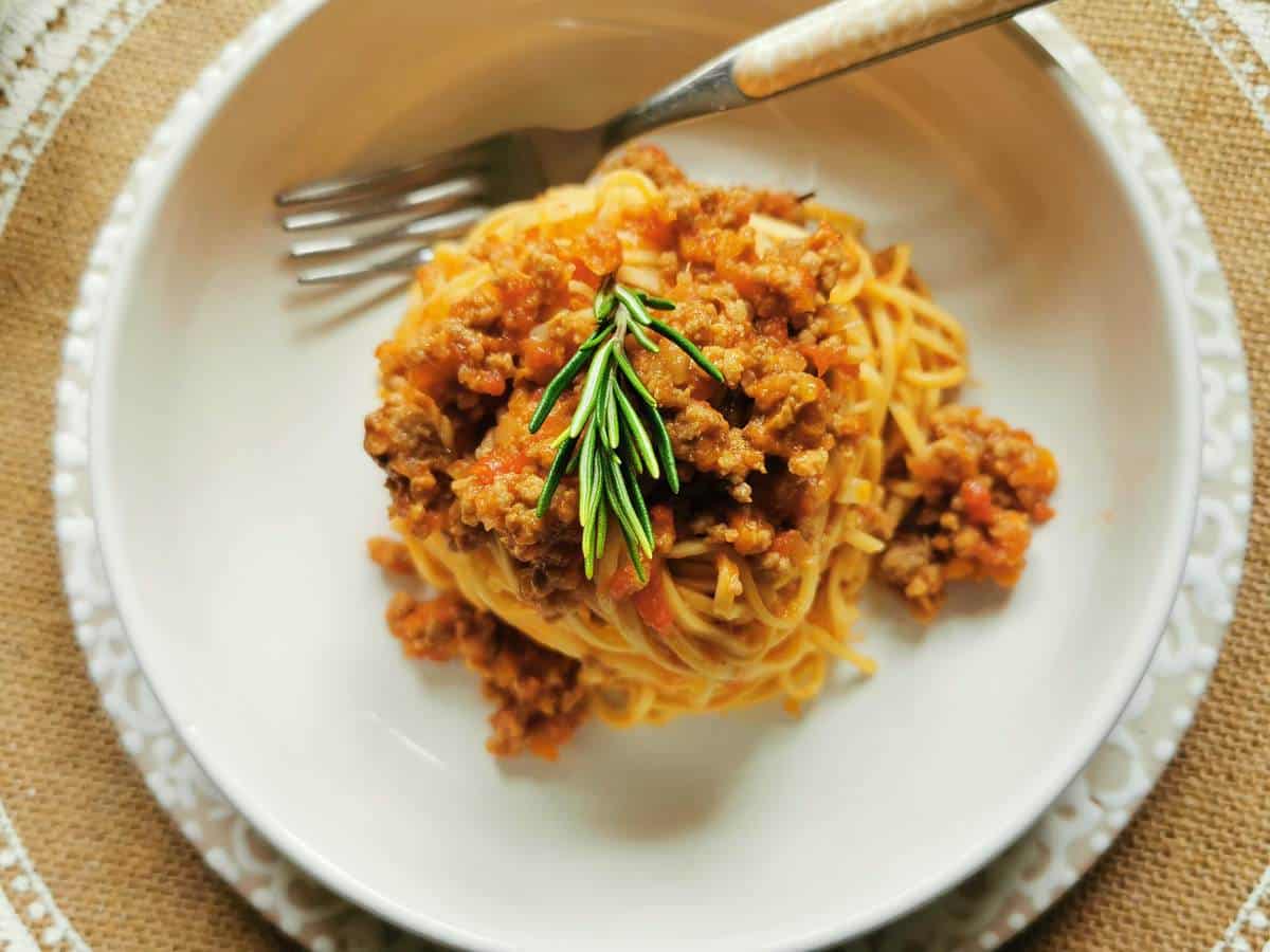 A serving of tajarin pasta with beef sausage ragu in a white bowl with a fork.