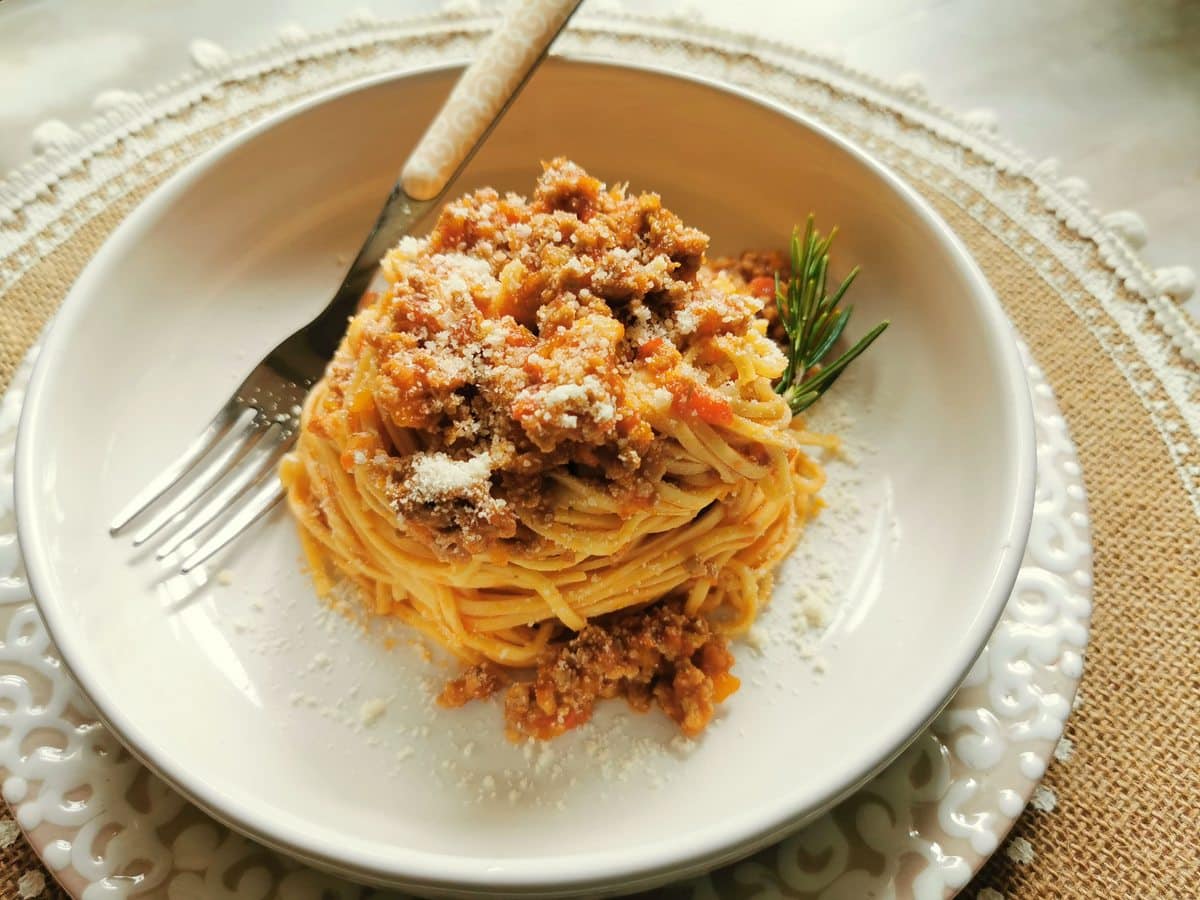 Serving of tajarin pasta with beef sausage ragu with parmigiano cheese sprinkled on top.