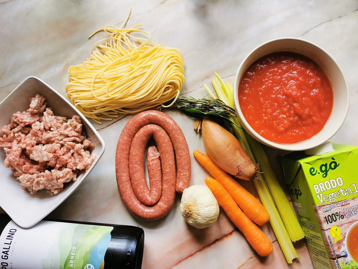 Ingredients for beef sausage ragu on pink marble work top.