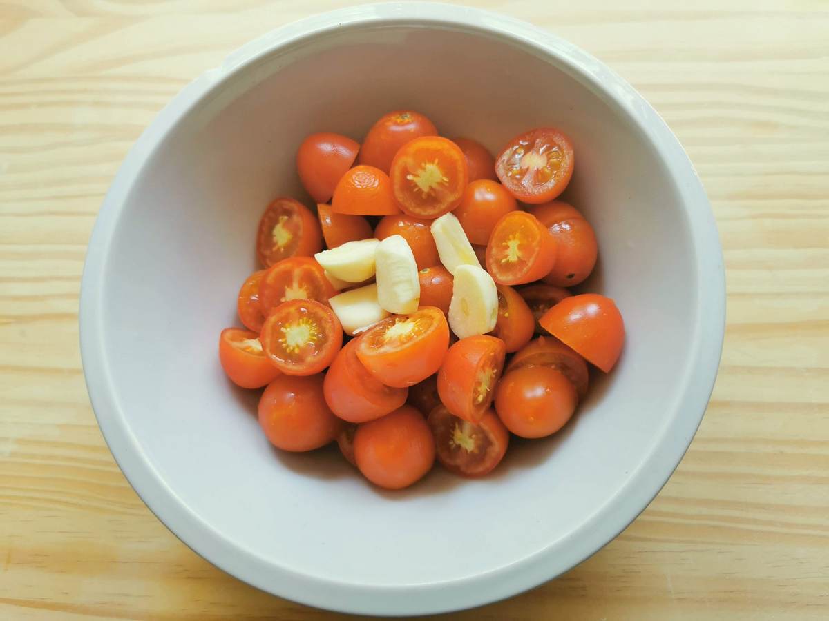 washed and halved small tomatoes and peeled garlic cloves in white bowl.