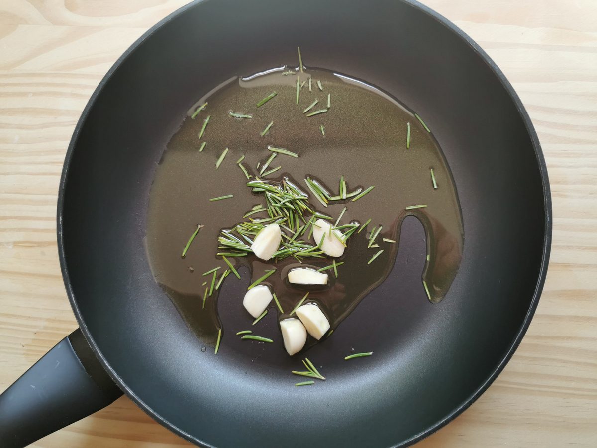 Peeled garlic cloves and chopped fresh rosemary leaves with olive oil in skillet.