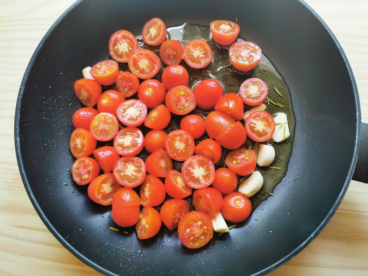 Halved small tomatoes with rosemary and garlic in skillet.